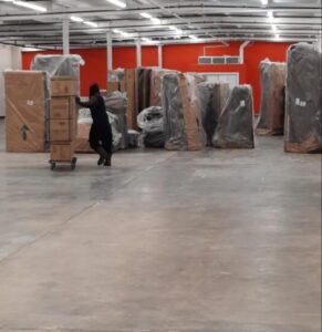 Muscle 4 Moving mover pushing inventory on a dolly in Huntsville Furniture Outlet 35816.