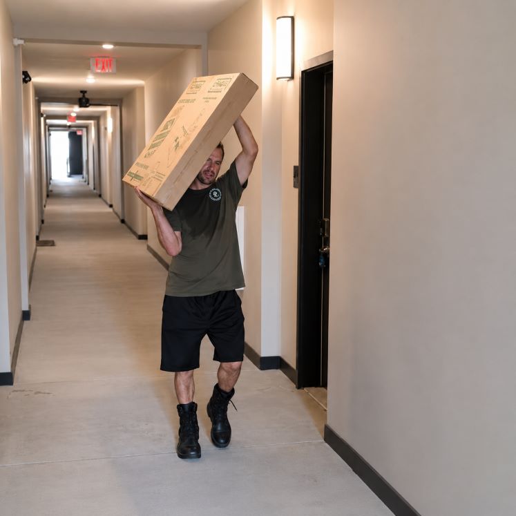 Muscle 4 Moving Apartment mover carrying a large box through the hallway at Arcadia Luxury Apartments during a residential move in Huntsville AL