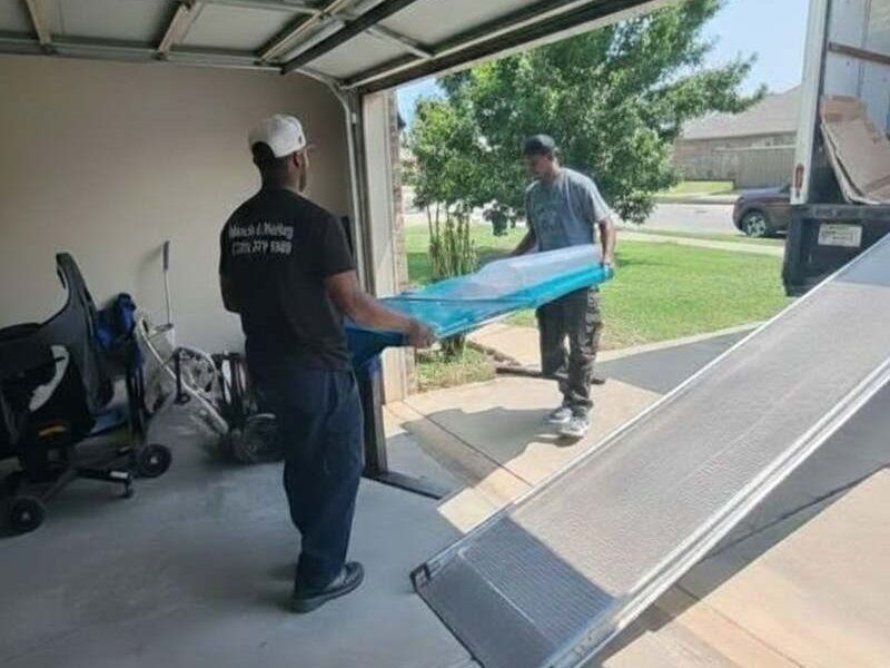Two home movers carrying a wrapped piece of furniture from the company truck into a home in Madison AL 35756